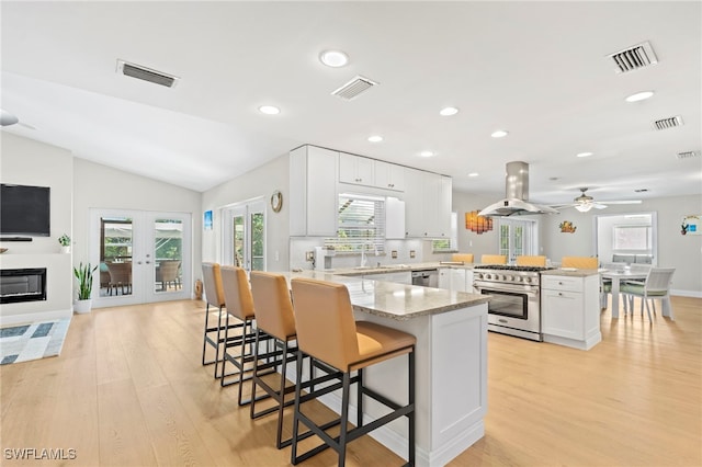 kitchen featuring island exhaust hood, kitchen peninsula, light hardwood / wood-style floors, white cabinets, and appliances with stainless steel finishes