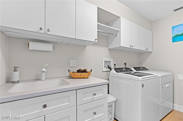 laundry area with cabinets, sink, light hardwood / wood-style floors, and washing machine and clothes dryer