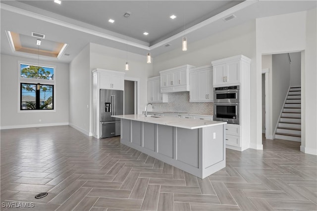 kitchen with appliances with stainless steel finishes, a center island with sink, a raised ceiling, and white cabinetry