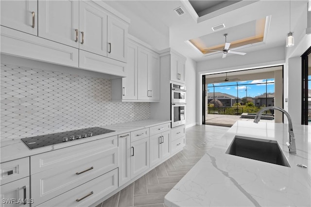 kitchen featuring white cabinets, black stovetop, hanging light fixtures, and sink