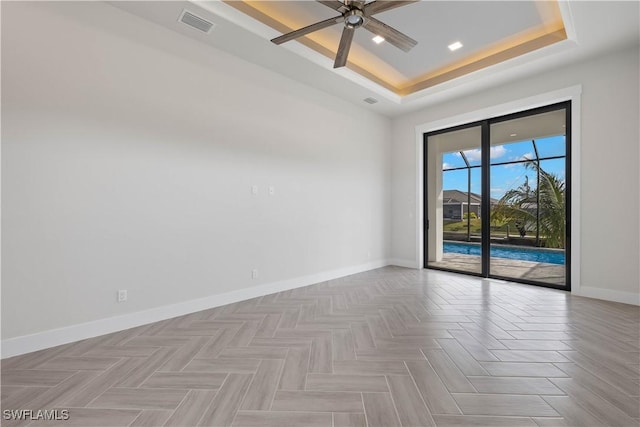 spare room with a raised ceiling, light parquet floors, and ceiling fan