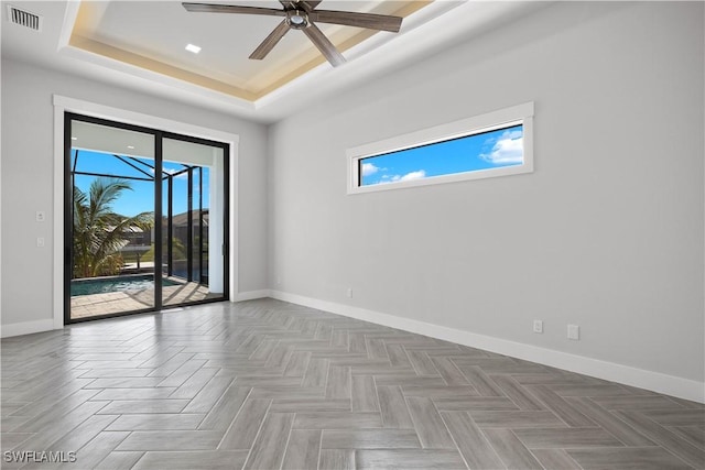 unfurnished room featuring ceiling fan, parquet flooring, and a tray ceiling