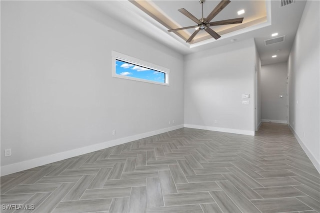 spare room featuring a tray ceiling, light parquet floors, and ceiling fan