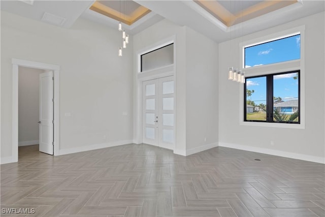 unfurnished room featuring light parquet flooring, a raised ceiling, a towering ceiling, and french doors