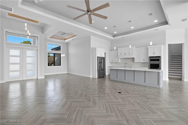 kitchen featuring white cabinetry, hanging light fixtures, stainless steel appliances, a raised ceiling, and an island with sink