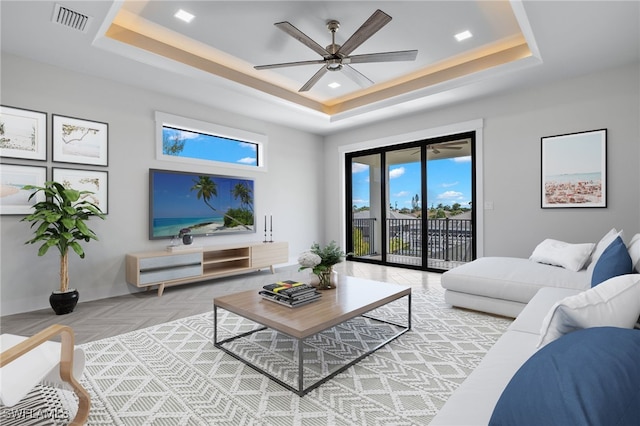 living room with a tray ceiling, ceiling fan, and parquet floors