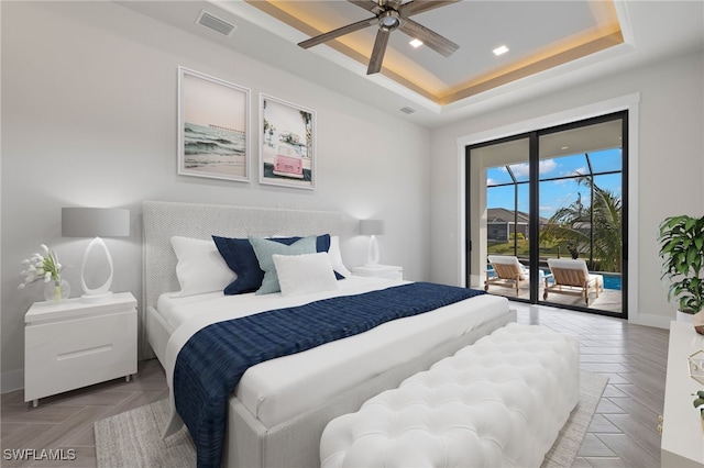 bedroom with access to exterior, a tray ceiling, parquet floors, and ceiling fan