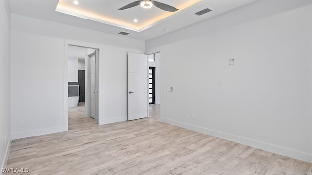 spare room with ceiling fan, a raised ceiling, and light hardwood / wood-style flooring