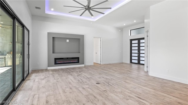 unfurnished living room with light hardwood / wood-style flooring, ceiling fan, a towering ceiling, a tray ceiling, and french doors