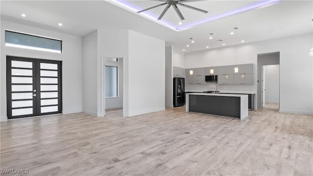 kitchen with gray cabinets, decorative light fixtures, a kitchen island with sink, black fridge, and light hardwood / wood-style flooring