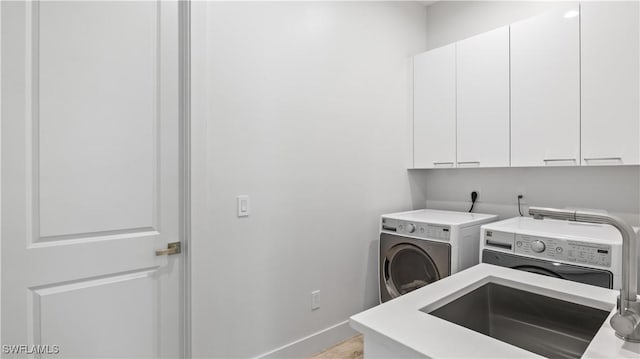 clothes washing area with sink, washer and clothes dryer, and cabinets