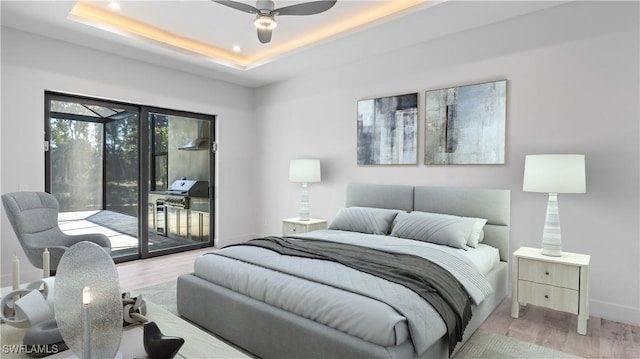 bedroom featuring ceiling fan, access to exterior, light hardwood / wood-style floors, and a tray ceiling