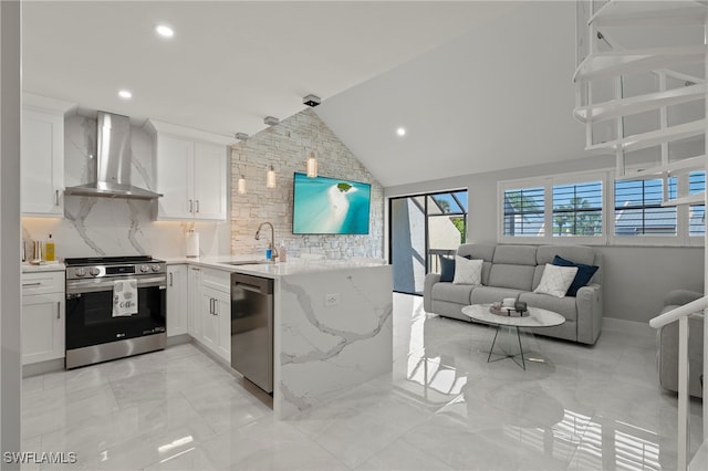 kitchen featuring sink, vaulted ceiling, wall chimney exhaust hood, white cabinetry, and stainless steel appliances