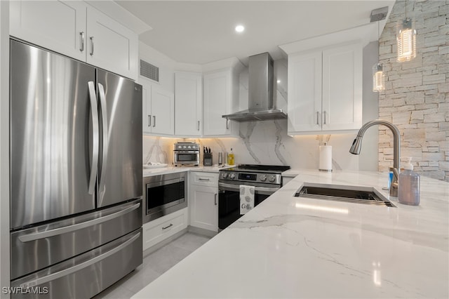 kitchen with light stone counters, stainless steel appliances, sink, wall chimney range hood, and white cabinets