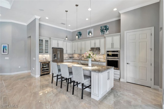 kitchen featuring a center island with sink, light stone counters, a towering ceiling, and wine cooler