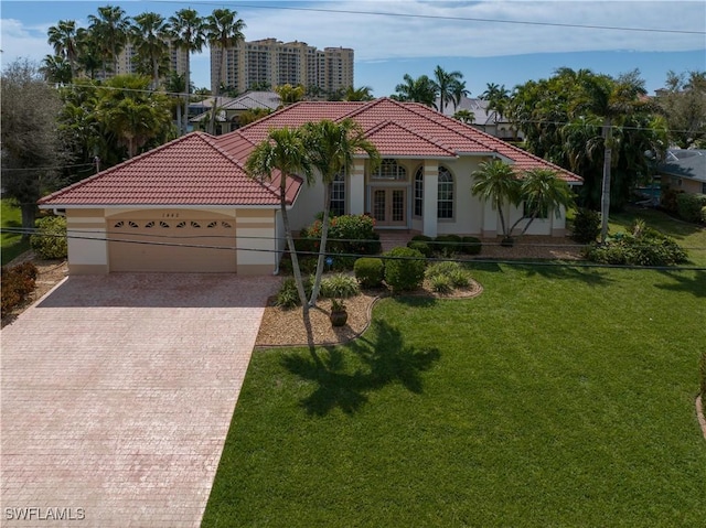 mediterranean / spanish home with an attached garage, a tiled roof, decorative driveway, stucco siding, and a front yard