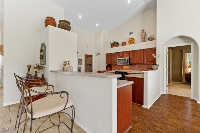 kitchen with kitchen peninsula, decorative backsplash, hardwood / wood-style flooring, high vaulted ceiling, and black range with electric stovetop