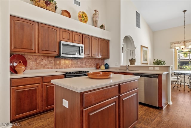 kitchen with high vaulted ceiling, dark hardwood / wood-style floors, decorative light fixtures, a kitchen island, and appliances with stainless steel finishes