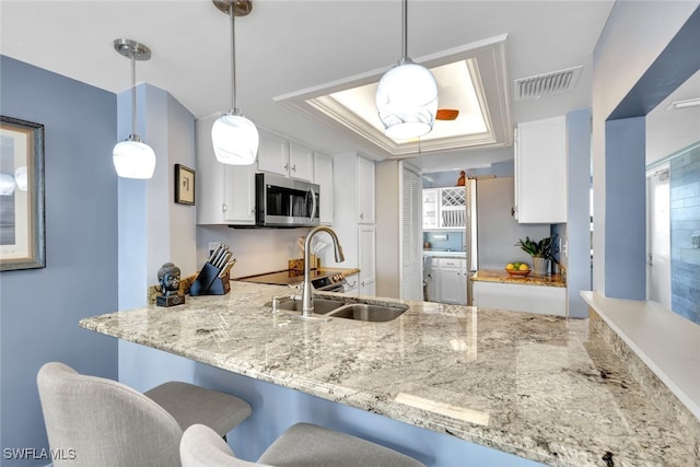 kitchen featuring pendant lighting, a raised ceiling, sink, and white cabinets