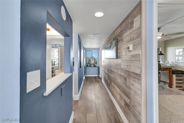 corridor featuring a healthy amount of sunlight, wooden walls, and light hardwood / wood-style floors