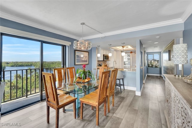 dining area featuring crown molding, a water view, sink, and light hardwood / wood-style flooring