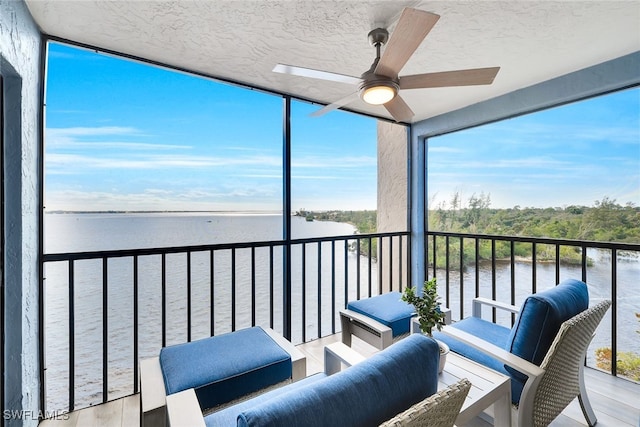 sunroom with ceiling fan and a water view