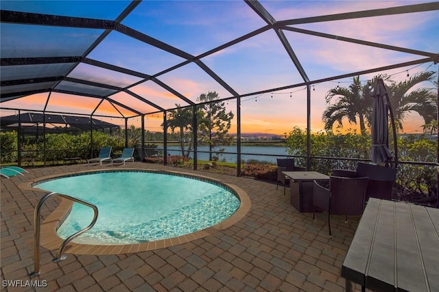 pool at dusk featuring a patio, a water view, and a lanai