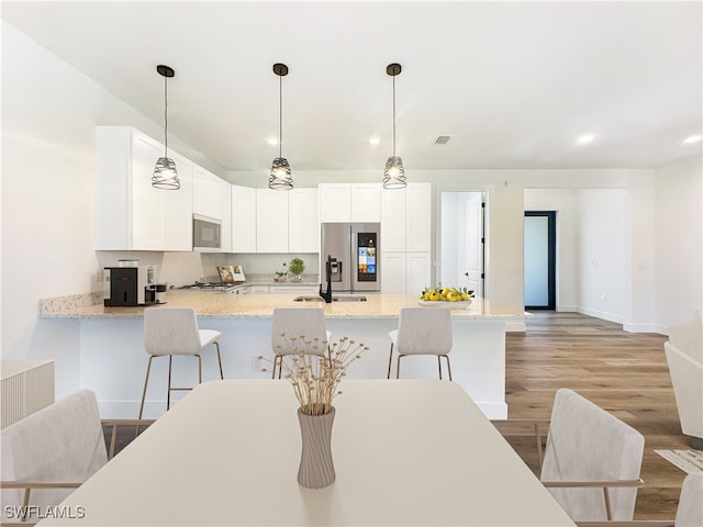 kitchen featuring a breakfast bar, white cabinets, light stone countertops, light hardwood / wood-style floors, and stainless steel appliances