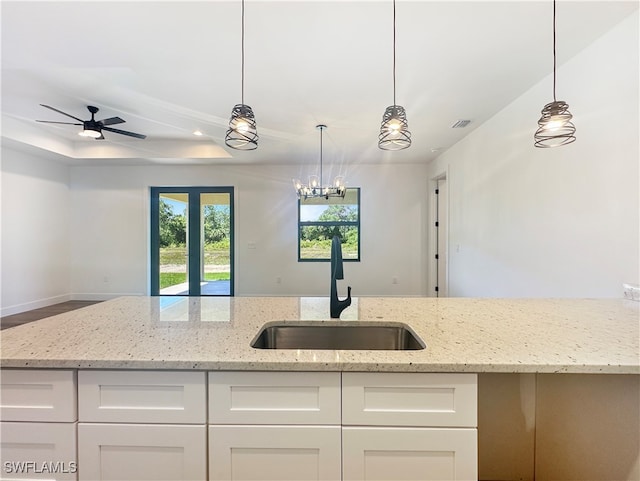 kitchen featuring light stone countertops, ceiling fan, sink, white cabinets, and hanging light fixtures