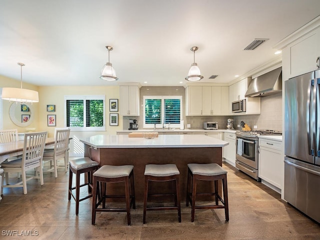 kitchen with white cabinetry, a kitchen island, stainless steel appliances, and wall chimney range hood