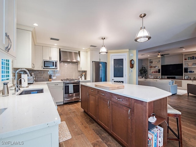 kitchen featuring sink, wall chimney exhaust hood, dark hardwood / wood-style flooring, pendant lighting, and appliances with stainless steel finishes