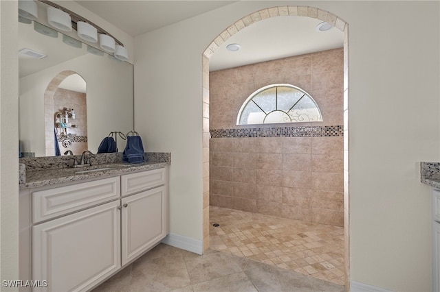 bathroom featuring tile patterned flooring, a tile shower, and vanity