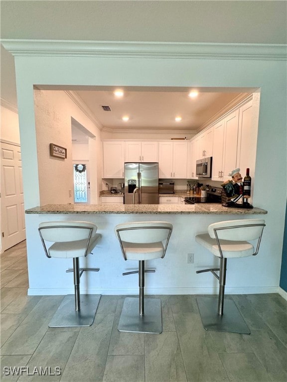 kitchen featuring kitchen peninsula, a kitchen bar, stainless steel appliances, and white cabinetry