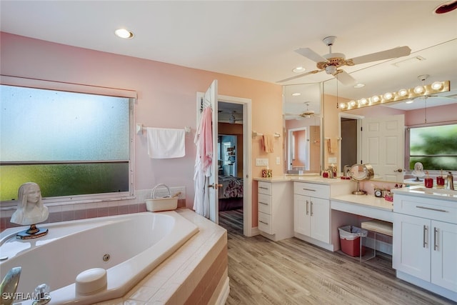 bathroom with hardwood / wood-style floors, vanity, ceiling fan, and tiled bath