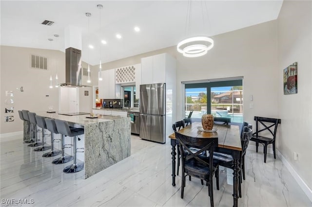 kitchen with appliances with stainless steel finishes, decorative light fixtures, white cabinetry, and wall chimney range hood