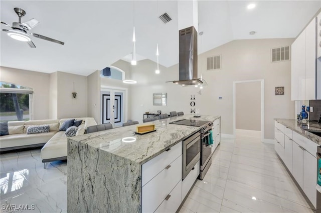 kitchen with light stone countertops, a kitchen island, stainless steel stove, white cabinetry, and range hood