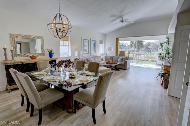 dining area featuring ceiling fan with notable chandelier, vaulted ceiling, a wealth of natural light, and light hardwood / wood-style flooring