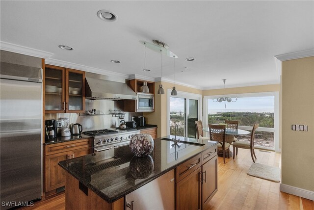 kitchen with a healthy amount of sunlight, built in appliances, wall chimney exhaust hood, and pendant lighting