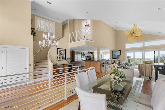 dining space with hardwood / wood-style floors, ceiling fan with notable chandelier, a towering ceiling, and crown molding