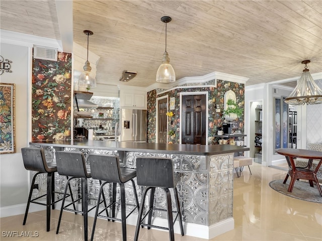 kitchen featuring white cabinets, decorative light fixtures, stainless steel fridge, and a breakfast bar