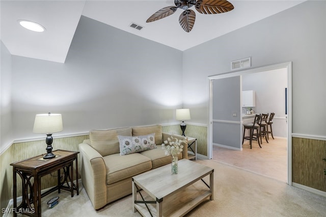 living room featuring light carpet, ceiling fan, and wooden walls