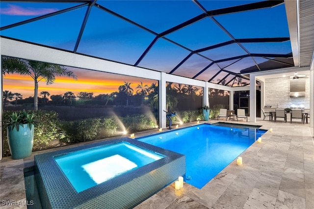 pool at dusk with glass enclosure, ceiling fan, a patio area, and an in ground hot tub