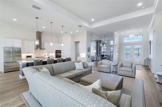 living room featuring an inviting chandelier, french doors, sink, crown molding, and light wood-type flooring