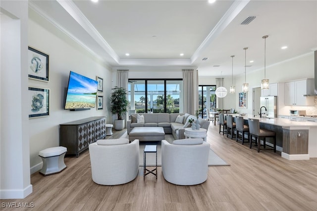 living area with light wood-style flooring, a tray ceiling, visible vents, recessed lighting, and ornamental molding