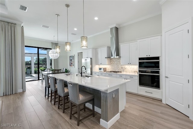 kitchen featuring white cabinetry, wall chimney range hood, a large island with sink, pendant lighting, and appliances with stainless steel finishes