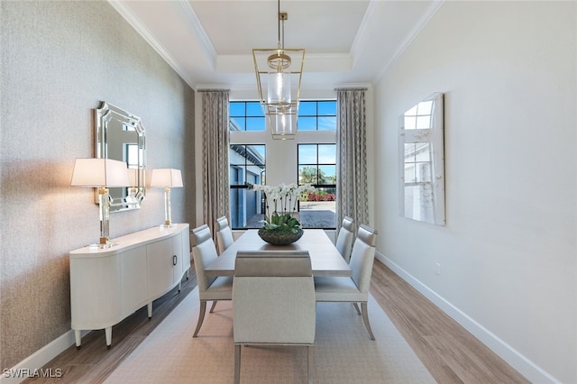 dining area featuring hardwood / wood-style flooring, a raised ceiling, ornamental molding, and an inviting chandelier