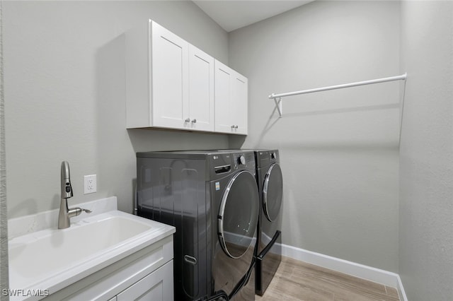 washroom with cabinets, light hardwood / wood-style floors, washing machine and dryer, and sink