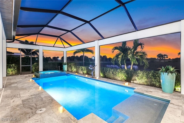 pool at dusk with glass enclosure, a patio area, and an in ground hot tub