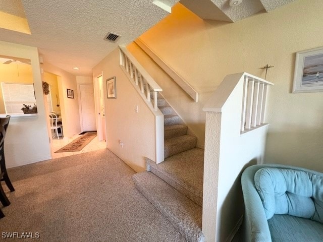 stairway featuring a textured ceiling and carpet floors