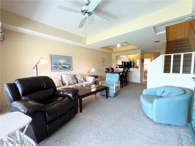 living room featuring light carpet, a textured ceiling, a tray ceiling, and ceiling fan